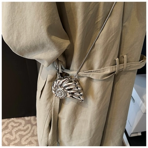 Silver nautilus shell mini bag with snake chain worn over a khaki trench coat
