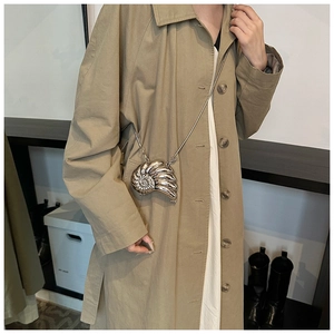 Silver metallic seashell clutch bag with chain strap shown on a trench coat model