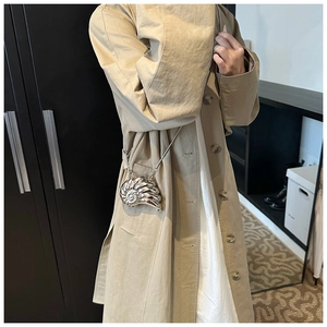 Close-up of a mini shell-shaped silver metallic crossbody bag with fine chain on a trench coat