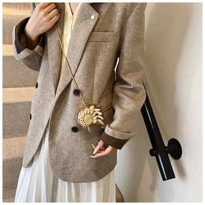 Mini golden conch shell crossbody bag with metallic chain on elegant model outfit
