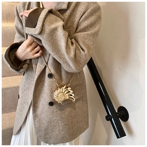 Golden shell-shaped mini crossbody bag with fine metal chain strap shown on a model
