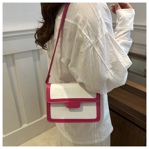 Close-up of crocodile textured crossbody bag with fuchsia trim worn by a model