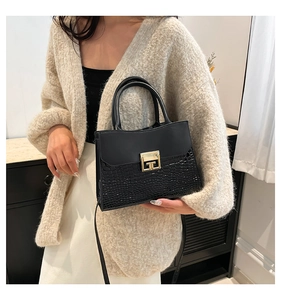 Dettaglio borsa nera con trama a coccodrillo e fibbia dorata su maglione in maglia beige