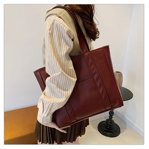 Detailed side view of large burgundy faux leather tote bag worn by a model