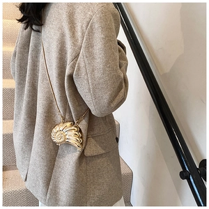 Golden seashell crossbody bag with metal chain shown on model in a stylish suit