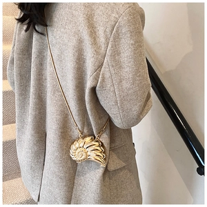 Detail of golden seashell chain bag worn by model showing luxury metallic shell design