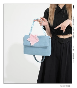 Detail of light blue denim handbag with pink frayed star patch and resin chain handle