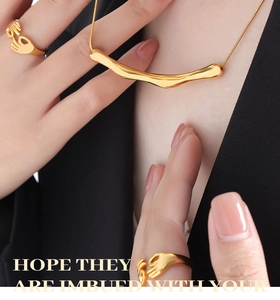 Détail du collier doré irrégulier et des bagues mains en prière portés par un mannequin