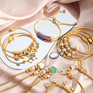 Gold evil eye heart and butterfly charm bracelets displayed on pink satin with reflection