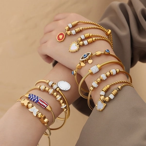 Gold-plated bracelet set with butterfly, evil eye, and heart charms on a warm sandy background