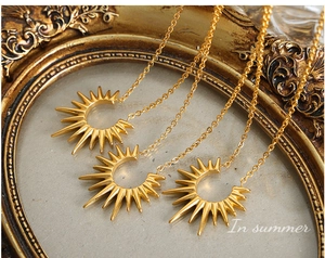 Détail de colliers avec pendentif soleil doré présentés sur un cadre doré vintage