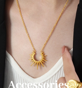 Détail du pendentif soleil doré et chaîne o-link portés avec une bague en relief