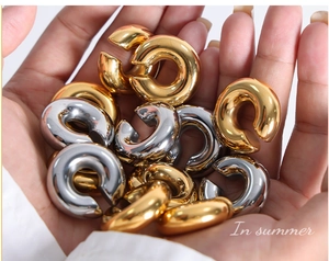 Gros plan de boucles d'oreilles créoles C épaisses en acier titane poli or et argent