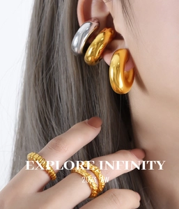 Gros plan de boucles d'oreilles et bagues texturées dorées sur un modèle au style moderne