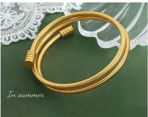 Détail d'un bracelet spirale doré multicouche sur un fond texturé vert foncé élégant