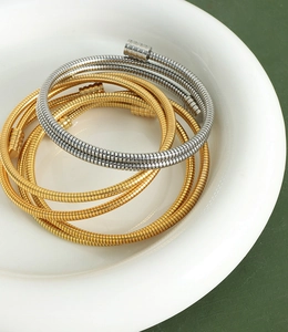 Gros plan détaillé de bracelets serpentins dorés et argentés dans un plat en céramique