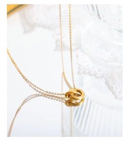Primer plano del collar con colgante de dos anillos entrelazados en oro sobre espejo
