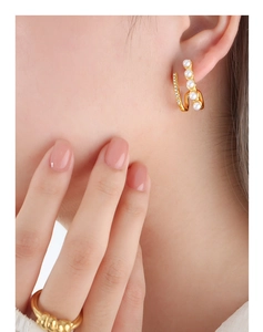 Macro detail of wave-shaped gold earrings with gradient pearls and crystal zircon