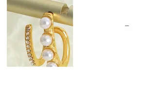 Detailed view of gold C-shaped earrings with inlaid white pearls and small cubic zirconia