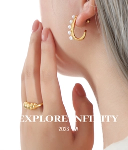 Close-up of gold C-shaped hoop earrings with pearls and a twisted ring on a model