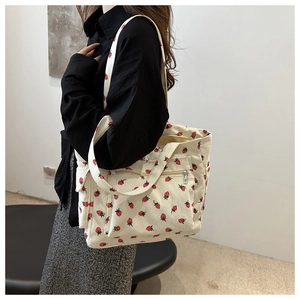 Detail of corduroy tote bag featuring red strawberry prints and front zipper pocket
