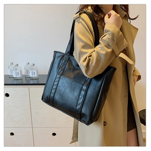 Fashionable black tote bag with wrinkled texture worn by model in trench coat