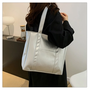 Silver metallic tote bag with high-gloss leather texture worn on shoulder by a model