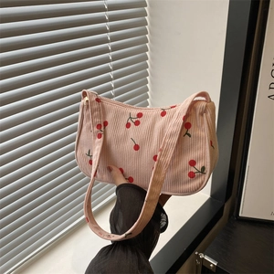 Pink corduroy baguette bag with cherry print held by hand against minimalist background