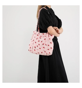 Detail of pink corduroy tote bag with red strawberry pattern shown on shoulder