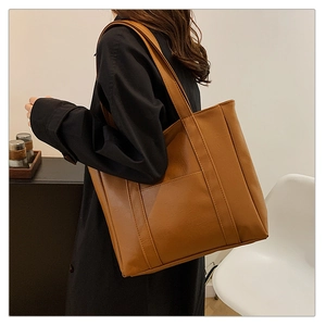 Close-up of a large brown PU leather tote bag featuring elegant vertical strap details