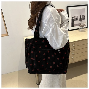 Detail of black corduroy tote bag with red strawberry print and zipper outer pocket