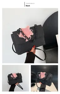 Detail of black denim shoulder bag with pink frayed star patch and black chain decor