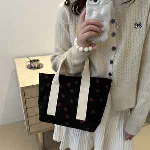 Cute black corduroy handbag with strawberry embroidery and white handles shown by model