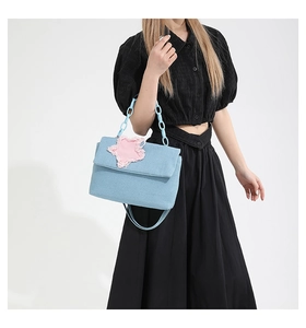 Close-up of light blue denim shoulder bag featuring a pink star patch and chunky chain handle