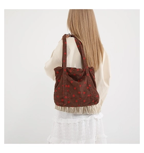 Detail of strawberry print on brown corduroy tote bag worn by a model