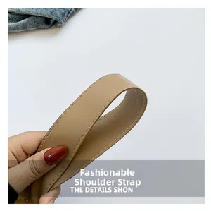 Détail de la bandoulière en cuir kaki avec surpiqûres fines sur fond en denim bleu