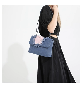 Detail of blue denim shoulder bag featuring a pink star patch and bold matte chain strap