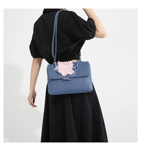Detail of denim shoulder bag with pink star patch and light blue plastic chain strap