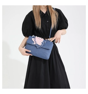 Detail of blue denim shoulder bag with pink frayed star patch and plastic chain