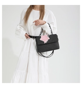 Detail of black denim handbag featuring a pink frayed star patch and matte chain strap