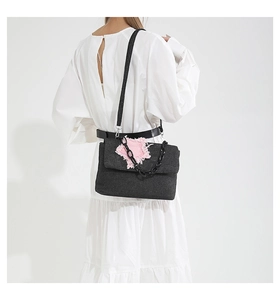 Macro shot of grey denim crossbody bag featuring a pink frayed heart patch and chunky chain