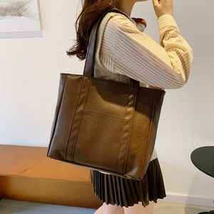 Brown faux leather tote bag with lychee texture shown on a female model in an indoor setting