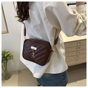 Detail of dark brown quilted crossbody bag with golden deer charm and wide strap