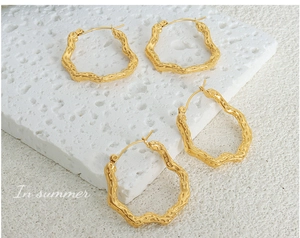 Close-up of golden irregular hollow earrings with hammered texture on white stone