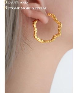 Close-up of chunky gold wavy hoop earrings with lava texture on a model side profile