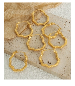 Macro detail of gold-plated geometric wavy earrings with hammered metal texture