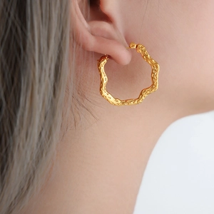 Irregular geometric gold-tone hoop earrings with hammered texture on a female model