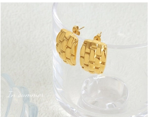 Macro shot of gold-plated rectangular earrings with textured lattice design on glass rim