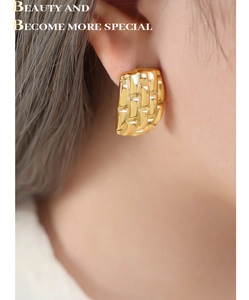 Macro detail of gold-plated geometric weave texture earring worn on a female ear