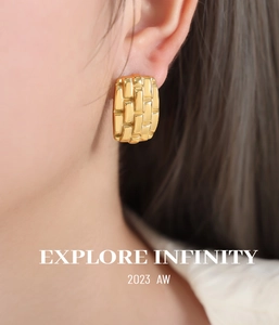 Close-up of gold rectangular earrings with woven texture on model's ear